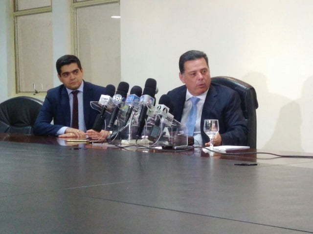 Homem de óculos sentado sorrindo e mexendo no celular 