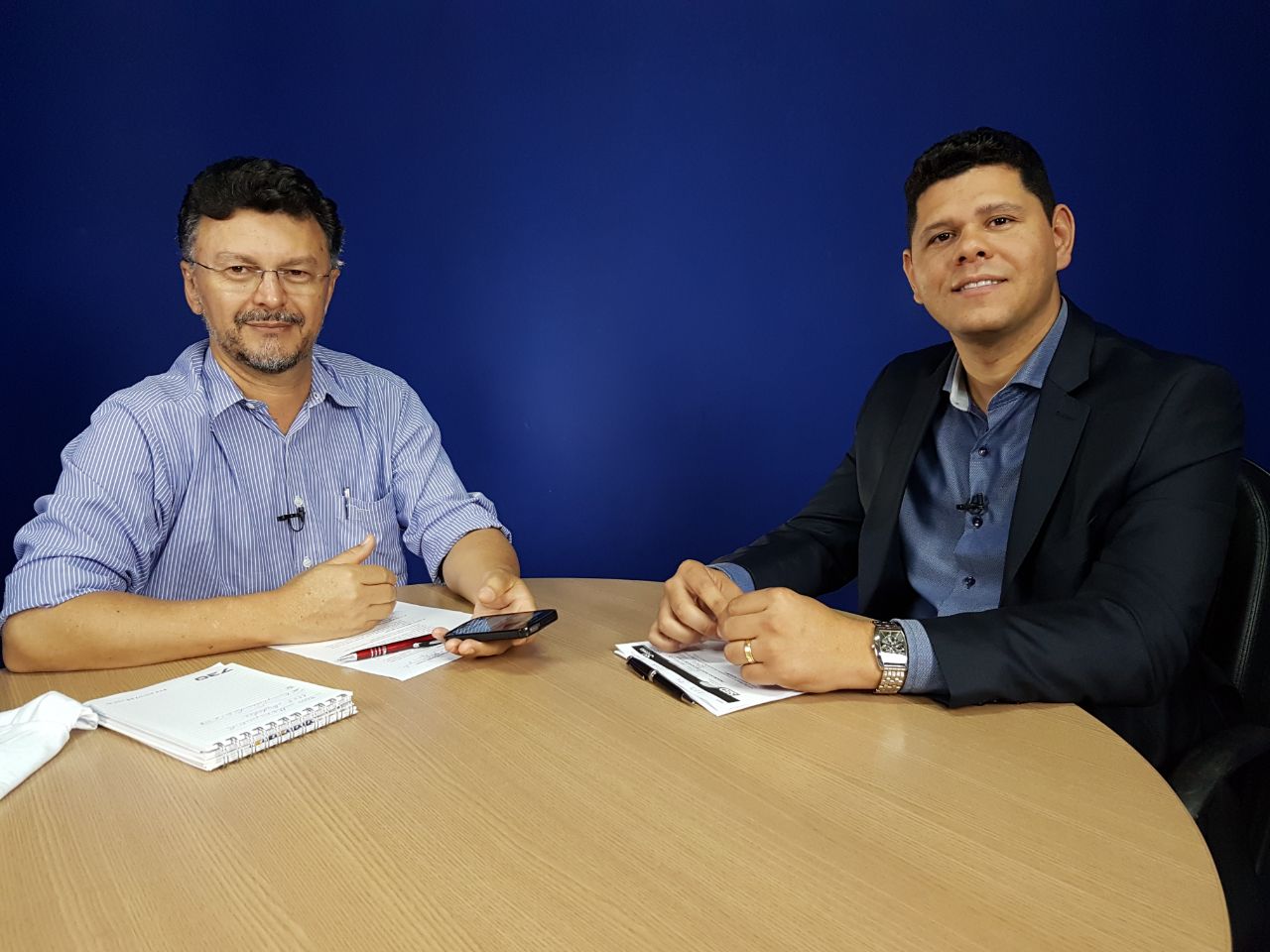 Copo de vidro com suco amarelo em cima de uma mesa de madeira com rodelas de laranja e uma banana 