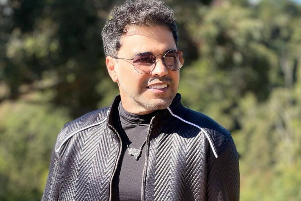 Homem e mulher um ao lado do outro segurando sacolas de compras, sorrindo e mexendo em um celular