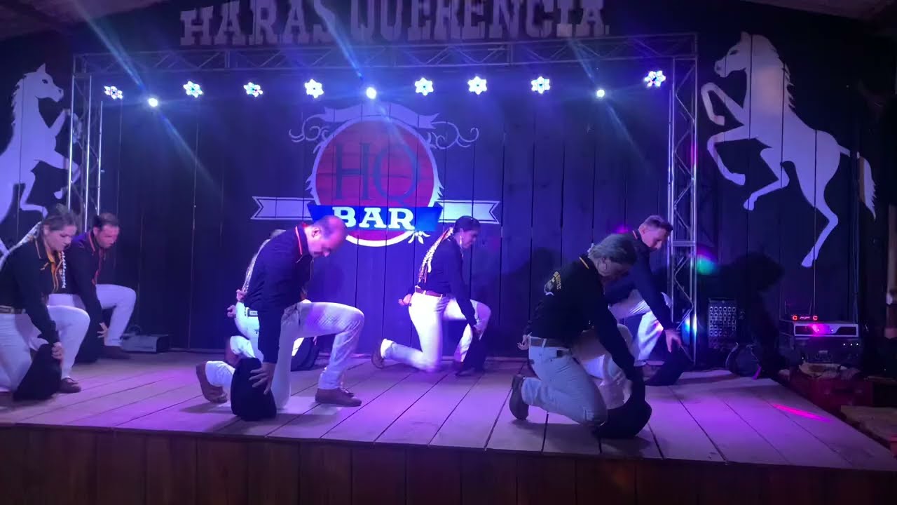 Mulher sentada em uma cadeira com um semblante feliz, ao lado está uma mesa com livros e um celular e, no parapeito da janela, há um vaso de plantas