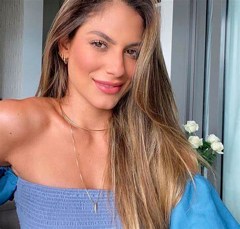 Mulher usando um uniforme azul ajudando uma idosa a se sentar em um sofá 