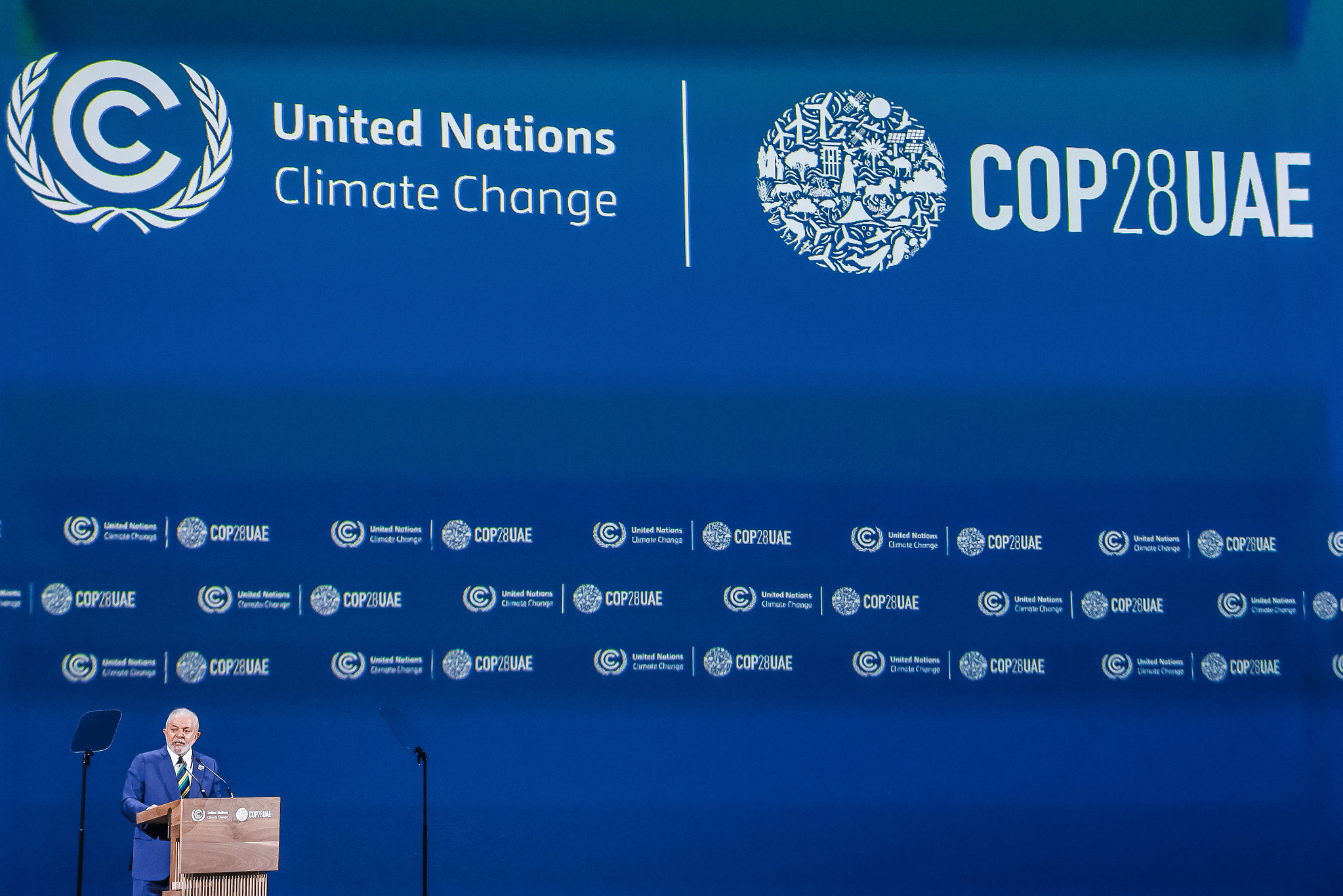 Mulher sorrindo, usando uma blusa amarela e posando para foto em um fundo azul-claro maquiando o rosto