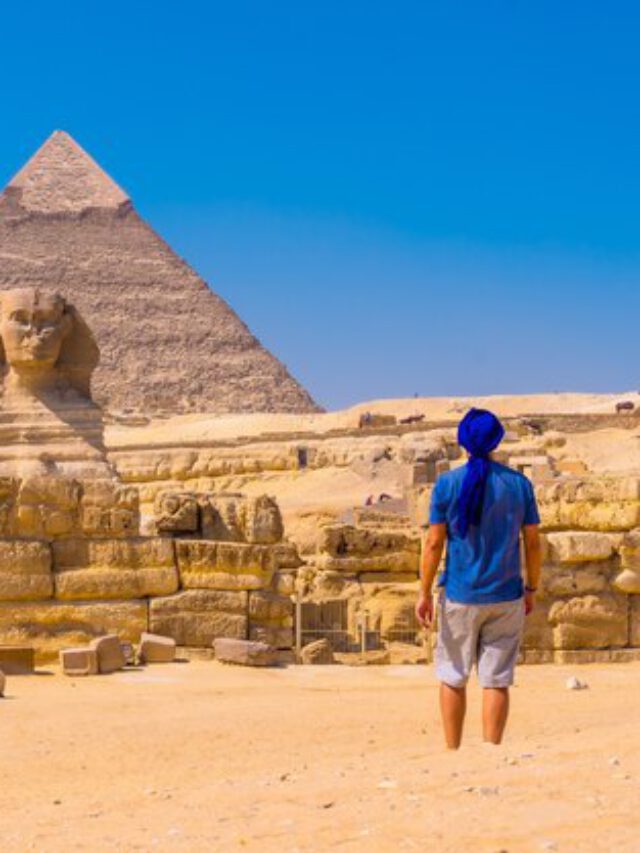 Mulher sorrindo e usando um chapéu bucket preto em frente a uma parede com azulejos coloridos 