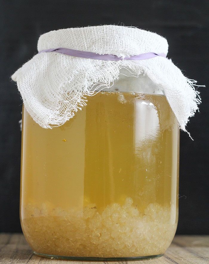 Mulher com o cabelo curto solto, usando uma blusa de frio marrom com as mãos unidas próximas ao rosto, orando de joelhos ao lado da cama e com uma bíblia. 