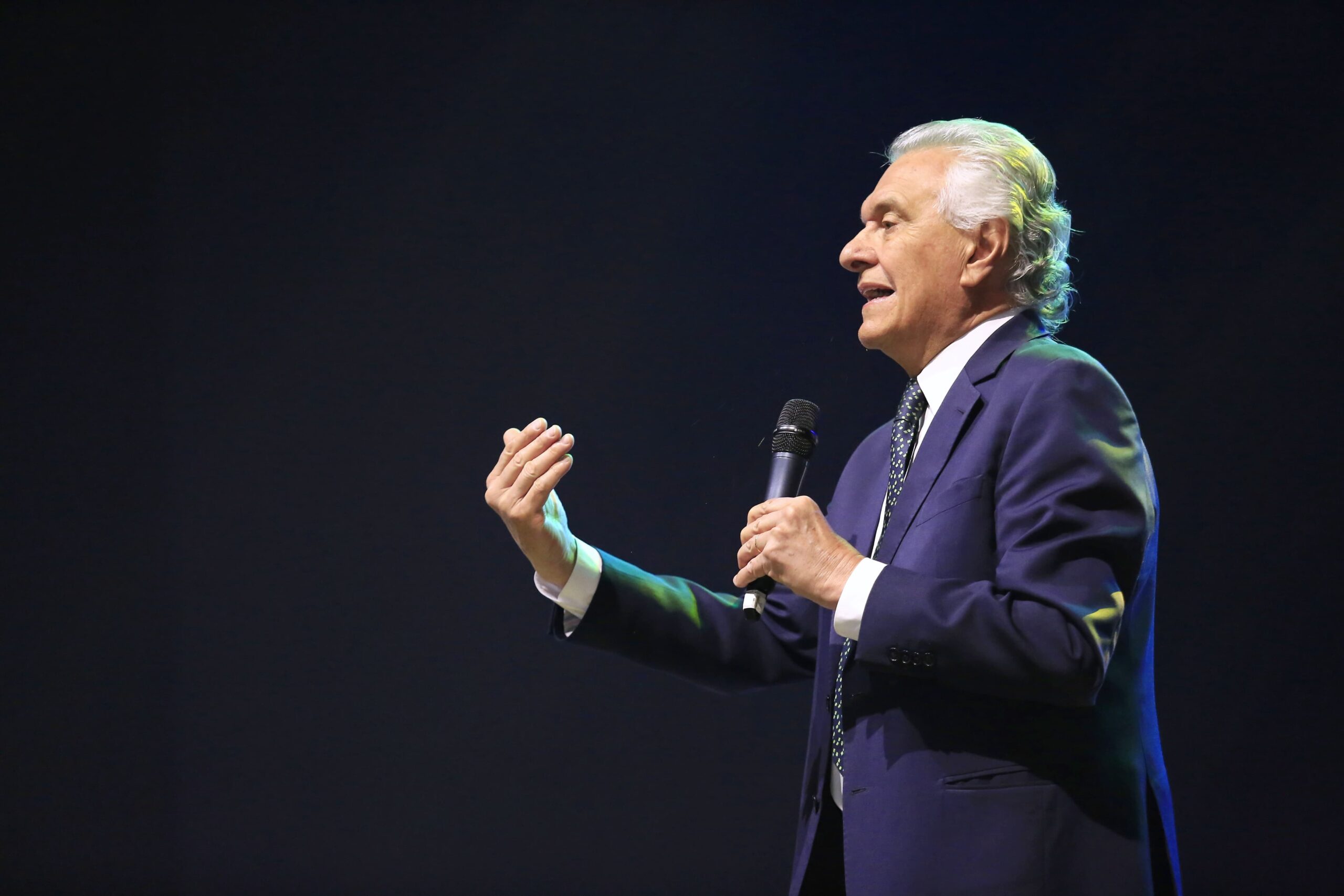 Mulher com cabelo loiro claro ondulado comprido e usando top preto em fundo bege