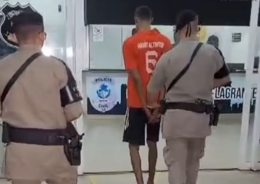 imagem com mulher no centro com vestido azul, duas pessoas atrás sentadas em cadeira e amarradas em faixas vermelhas e um homem e uma mulher atrás deles