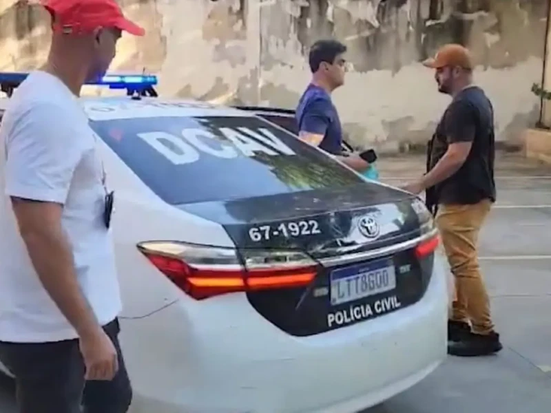 Ex-deputado é o que aparece sem boné, conduzido esta manhã para a delegacia por dois agentes Foto reprodução redes sociais