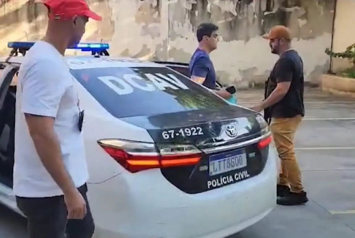 Ex-deputado é o que aparece sem boné, conduzido esta manhã para a delegacia por dois agentes Foto reprodução redes sociais